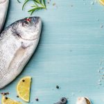 Fresh raw sea bream fish decorated with lemon slices, herbs and  shells on blue wooden background, copy spac