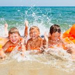 Three young boys laughing while splashing water at the beach