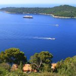 Above Idyllic Dubrovnik surroudings, green cypresses, italian pine trees, boat crossing water and yacht on bay of blue water  Dalmatia, Croatia